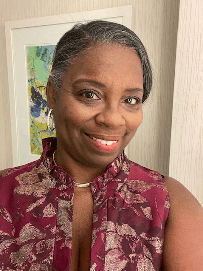 Smiling Black woman with grey hair wearing a maroon floral top and silver hoop earrings.